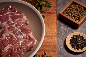 pork cheeks on a plate on a wooden board and next to different spices