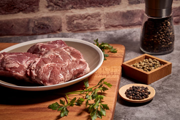 pork cheeks on a plate on a wooden board and next to different spices