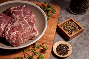 pork cheeks on a plate on a wooden board and next to different spices