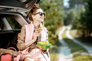 Young woman having a snack with lunch box while tarveling by car in the woods