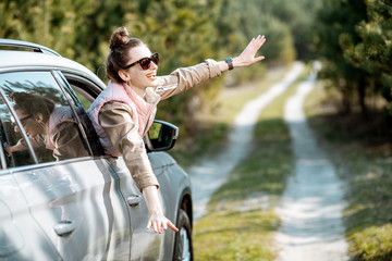 Young woman enjoying the trip, looking out the car window on a picturesque road in the woods