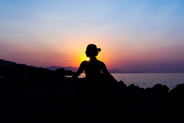 Silhouette of a young woman doing yoga on the beach at sunset.