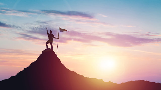 Man with flag celebrates victory on top of a mountain at sunset