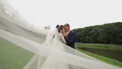 Groom with bride in bridal veil near lake in the park. Wedding couple