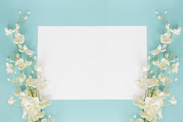Mothers day or wedding floral card with paper note and white flowers over a blue background shot from above. Flat lay. 