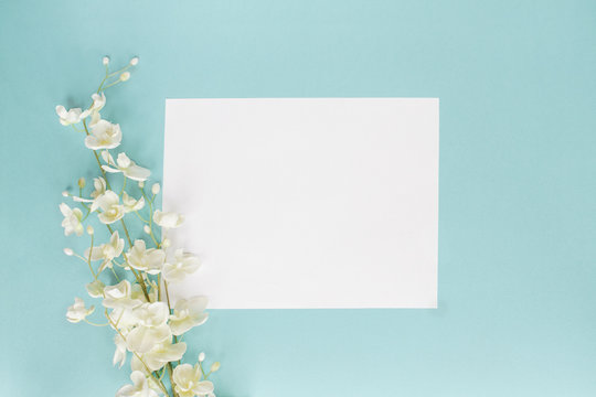 Mothers Day Or Wedding Floral Card With Paper Note And White Flowers Over A Blue Background Shot From Above. Flat Lay. 