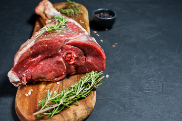 Raw leg of goat on a wooden cutting Board. Rosemary, thyme, black pepper. Black background, side...