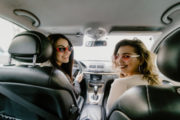 Perfect start of holidays. Rear view of two beautiful young cheerful women looking at each other with smile while sitting in car
