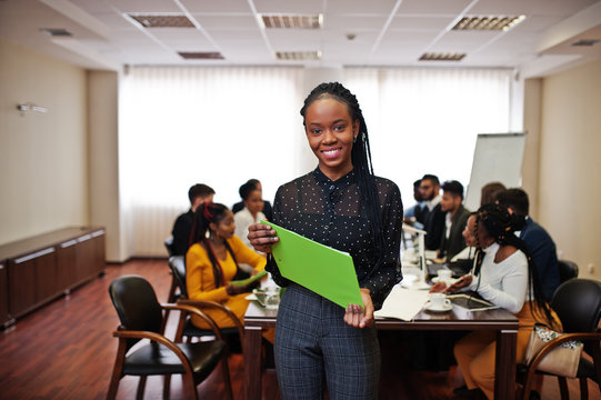 Face of handsome african business woman, holding clipboard on the background of business peoples multiracial team meeting, sitting in office table.