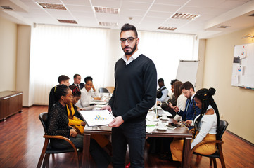 Face of handsome arabian business man, holding clipboard on the background of business peoples multiracial team meeting, sitting in office table.