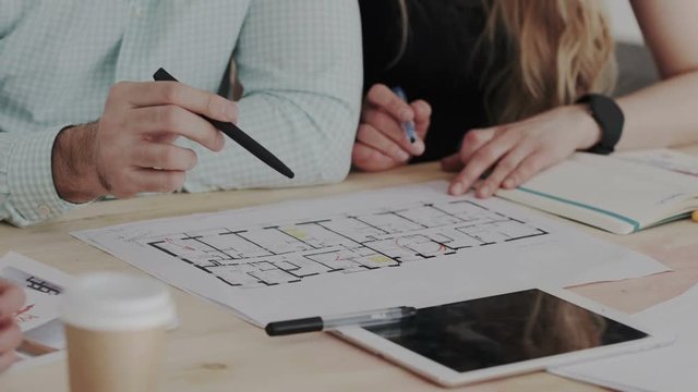 Close up shoot. Three skilled specialist discuss an architectural object. Workflow of creative interior designers with construction blueprint and illustrations.
