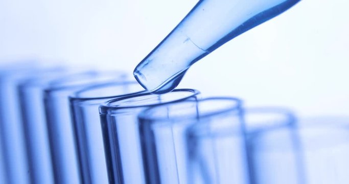 Chemical laboratory test, pipette drips transparent chemicals into blue test tubes. Chemical and medicine concept. Close-up side view.