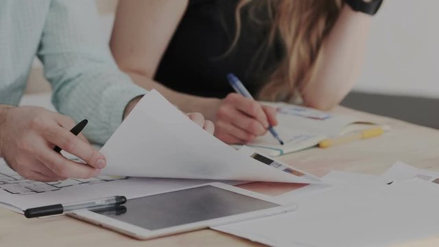 Closeup shoot. Male and female designers are discussing the location of interior objects. The man puts the picture and gestures. Woman writing in notebook