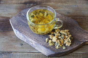  cup of chamomile tea with dry chamomile on a rustic wooden board