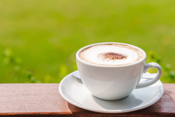 Hot coffee placed on the wooden table in early morning with copyspace, white cup and silver spoon. The green background with defocus effect.
