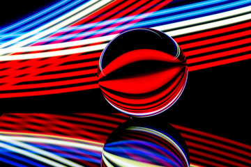 A glass crystal ball isolated against a black background with colorful streaks of neon light painting behind
