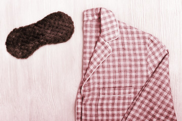 Red pajamas and sleep mask for comfort rest at night on white wooden background with copy space. Top view. Flat lay.