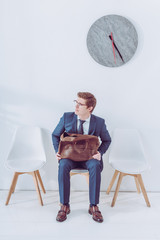 Fototapeta premium worried man in glasses holding briefcase while waiting job interview