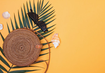 Stylish round straw handbag with palm leaf, sunglasses and seahells on the bright yellow background,