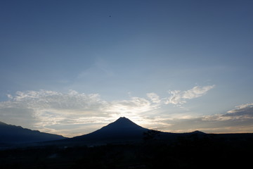 the view of the sun rises from behind the mountain, with a blue cloud background