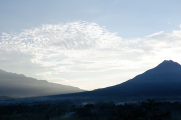 Fototapeta premium the view of the sun rises from behind the mountain, with a blue cloud background