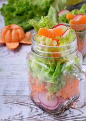 Layered salad in a jar with mandarins, radish, lettuce leaves, carrot and dressing