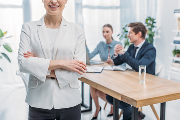 Fototapeta premium cropped view of cheerful recruiter standing with crossed arms near coworkers