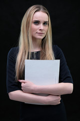 Studio portrait concept of a beautiful fashionable blonde business girl standing and talking in a business dress on a black background with a folder in hands.