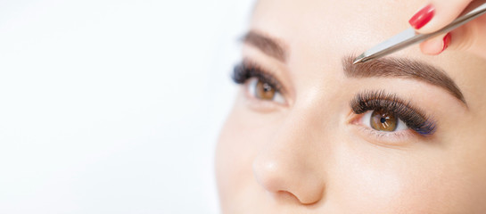 Beautiful young girl with long eyelashes tweezing her eyebrows in a beauty salon. Woman doing eyebrow permanent makeup correction . Microblading brow.