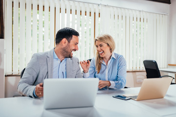 Two business partners laughing in bright office.