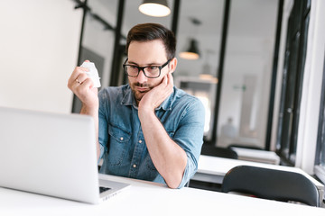 Annoyed casual man working in office while crumpling paper and looking at laptop.