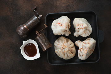 Georgian meat dumplings khinkali with dipping suace, flatlay over dark brown metal background, horizontal shot