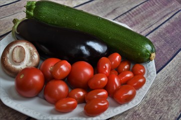 fresh whole vegetables, zucchini, eggplant, mushroom and mini tomatoes on a white plate