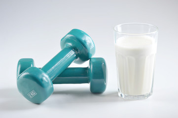 Two dumbbells and a glass of protein cocktail. White background. Close-up. The concept of sports and proper nutrition.