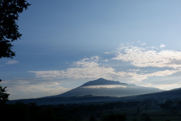 Fototapeta premium the view of the sun rises from behind the mountain, with a blue cloud background