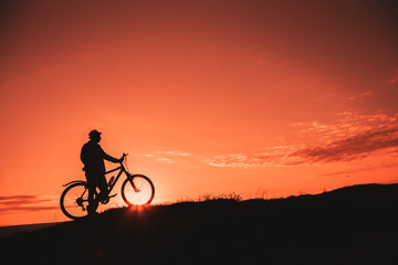 Naklejka na ściany i meble Silhouette of a male mountainbiker at sunset in the mountains