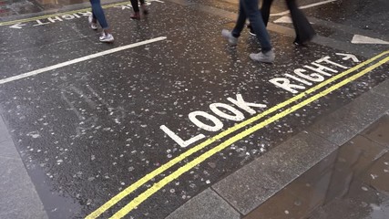 Pedestrians crossing road, "Look right" text on wet asphalt, detail on their legs only