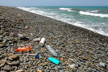 Fototapeta na wymiar Plastic bottles rubbish on wild pebbles beach. Ocean and sea littering concept