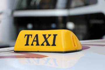Taxi light sign or cab sign in yellow color with black text on the car roof at the street blurred background.