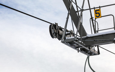 Steel ropes over wheels in mechanism on top of ski lift support pillar, number 5 on yellow plate. Wide banner with space for text left down