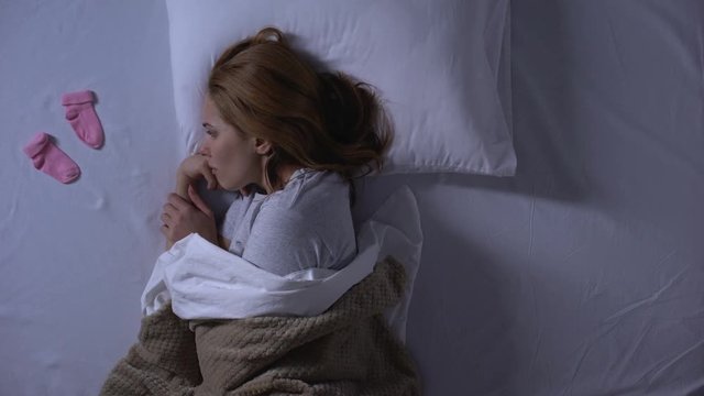 Lady crying hiding little baby socks under pillow, miscarriage, infertility