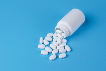 White pills, tablets and white bottle on blue background