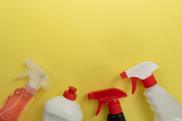 Tops of white, black and transparent plastic bottles of different detergents on yellow background. Spring house cleaning