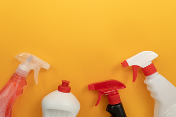 Tops of white, black and transparent plastic bottles of different detergents on orange background. Spring house cleaning