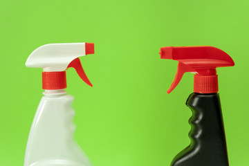 Close-up. White vs black spray bottles of cleaning products isolated on green background. Spring...