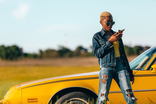 Black african woman looking at phone screen leaning on yellow cl