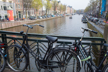 Fototapeta na wymiar Amsterdam/Netherlands, April 06, 2019: Old streets along numerous canals in Amsterdam. River transport and bicycles