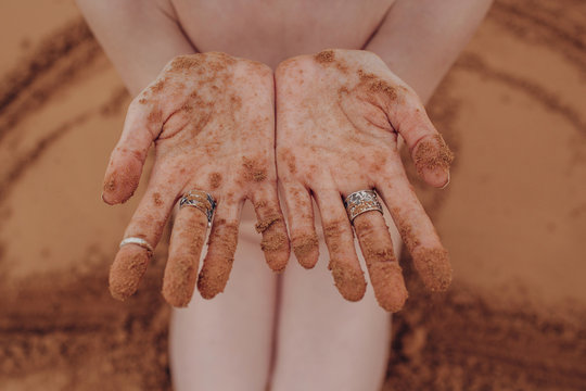 Crop photo of female's hands with silver rings covered with sand