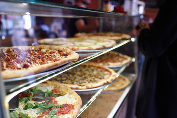 New York deli pizzas through a glass display case