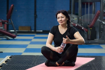 Senior woman in the gym sitting on a pink yoga mat. close-up. copy space.